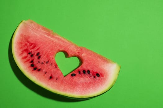 Ripe watermelon slice with heart shaped hole on green background, summer concept