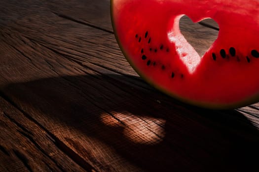 Ripe watermelon slice with heart shaped hole on blue background of the blue sky with little cloud on a hot summer day