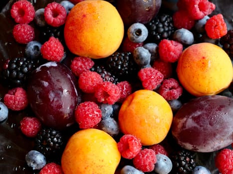 Colored background of seasonal summer fruits apricot, plum, raspberry, blueberry, blackberry in garden, close up