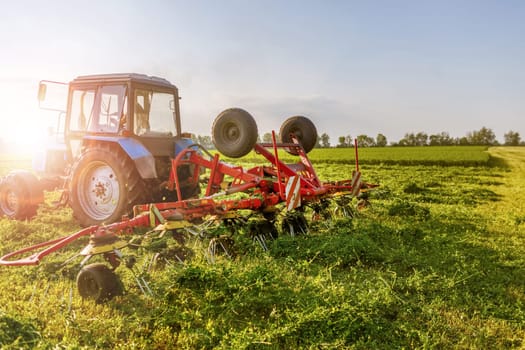 tractor harvesting hay for animals against the background of a field in the warm rays of the sun, agribusiness concept
