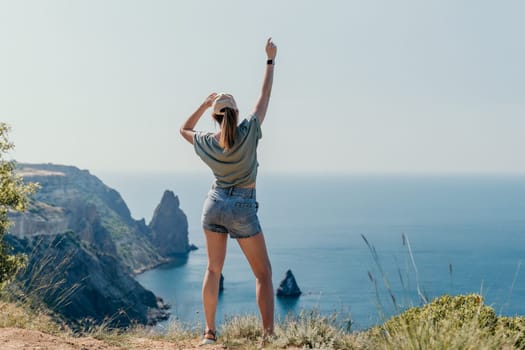 A young woman in a green shirt and denim shorts stands on a cliff overlooking a picturesque coastline.