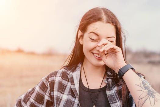 A woman is laughing with her hand covering her face, she's wearing a checkered shirt and has a tattoo on her arm.