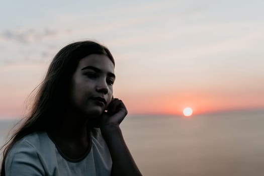 A young woman sits silhouetted against a colorful sunset, her expression contemplative.