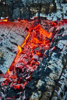 Image of Close up of glowing red embers wedged between three blackened logs and tiny flames background asset