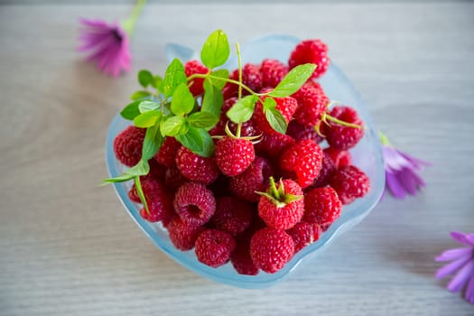 Fresh ripe raspberries in a glass bowl on a light wooden table.