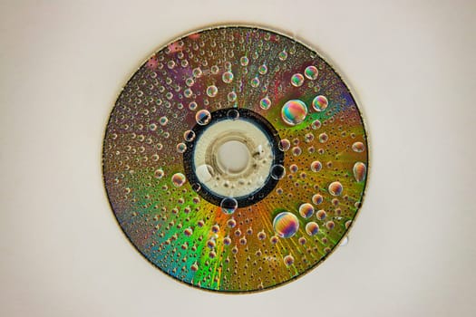 Image of CD on white background with rainbow water drops on reflective metal surface