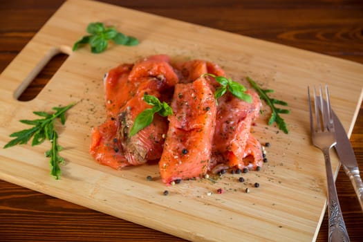 Fresh big pieces of salted red fish with spices and herbs on a wooden board.