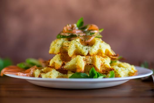 Cooked potato waffles with lightly salted red fish and herbs in a plate, on a wooden table.