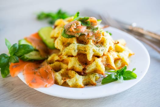 Cooked potato waffles with lightly salted red fish and herbs in a plate, on a wooden table.