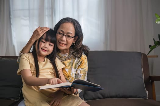 Grandma and granddaughter happily spend their free time reading books in the living room. An expression of love between an elderly woman and her adorable granddaughter..