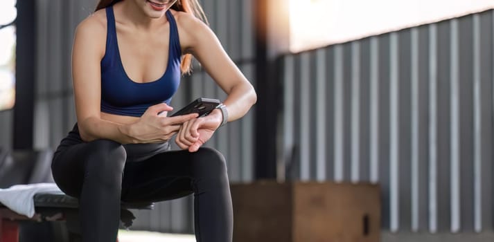 Young female athlete in sportswear sits at the gym using a cell phone while relaxing..