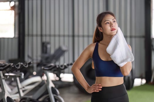 Young Asian woman stands and wipe her face after exercise at the gym..