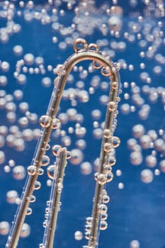 Image of Macro of silvery bubbles on paperclip with bubbly blue background