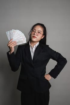 Young Asian woman holding a dollar bill in her hand standing on a gray background..