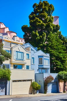 Image of Yellow and blue houses side by side on street with garage below bay windows