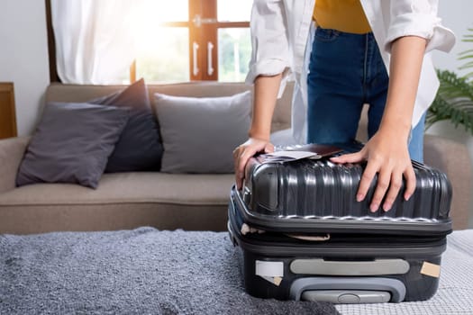 Woman tries to close a suitcase full of belongings in preparation for a holiday trip..