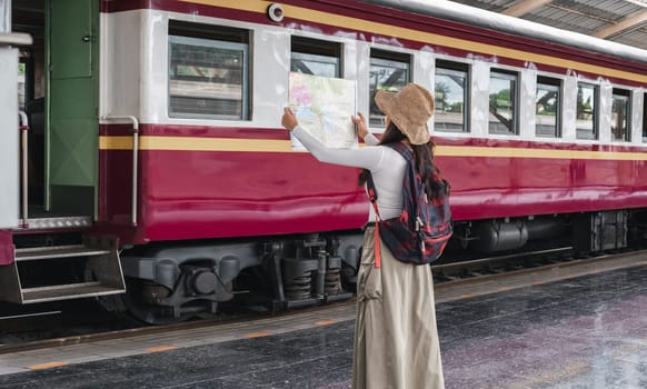 Young woman female smiling traveler with back pack looking to map while waiting for the train at train station..