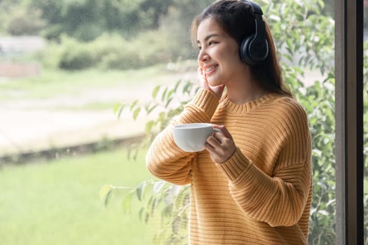 Portrait of beautiful young woman with a cup of coffee and wearing headphones standing relaxed and happy..