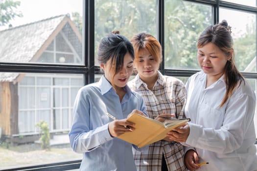 Asian College groups of students using laptop, tablet, studying together with notebooks documents paper for report near windows in classroom. Happy young study for school assignment