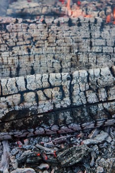 Image of Charred black log with white cracked ashen surface close up with small red embers background