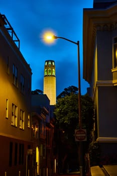 Image of Gorgeously illuminated Coit Tower at night seen from darkly lit ally street