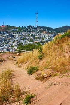 Image of Dirt trail winding down hillside to distant neighborhood under Sutro Tower