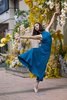 Beautiful Asian ballerina posing against the backdrop of a building decorated with flowers