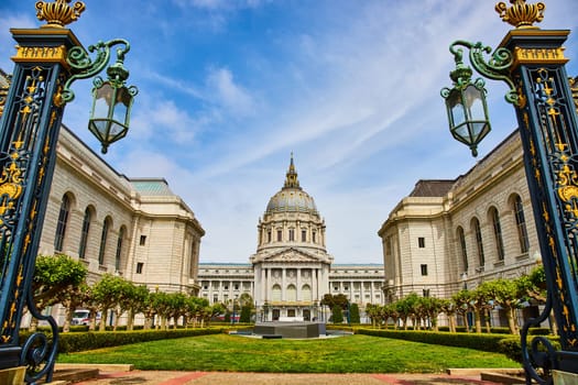Image of City hall with green courtyard framed by golden gilded lampposts with cloudy blue sky
