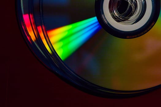 Image of Stacked CDs in dark setting with cone of rainbow colored light shaft across silvery surface
