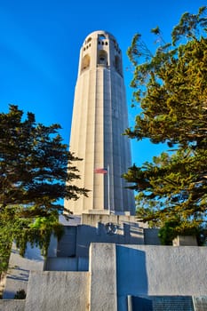Image of Coit Tower with memorial and American Flag under cerulean blue sky