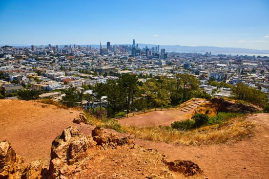 Image of Dirt park trail winding down hillside to San Francisco city and downtown with distant bay waters