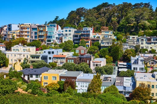 Image of Neighborhood of colorful houses on hill with trees and blue sky in background