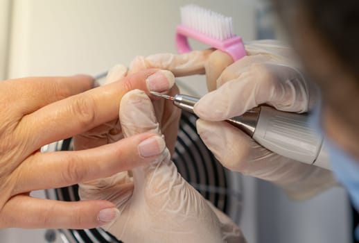 Nail care procedure in a beauty salon. Female hands and tools for manicure, process of performing manicure in beauty salon. Gloved hands of a skilled manicurist cutting cuticles. Concept spa body care