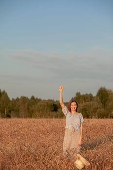 A young beautiful girl with braces on her teeth and long hair poses in a wheat field in the summer at sunset. The girl holds a hat in her hand against the background of a wheat field.
