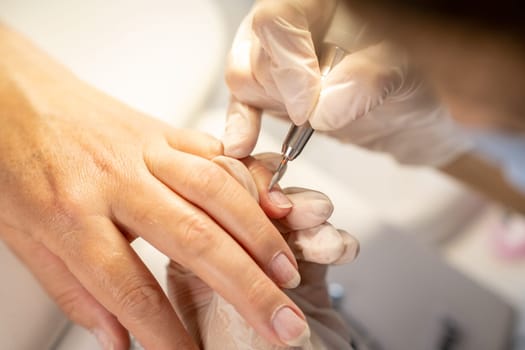 Nail care procedure in a beauty salon. Female hands and tools for manicure, process of performing manicure in beauty salon. Gloved hands of a skilled manicurist cutting cuticles. Concept spa body care