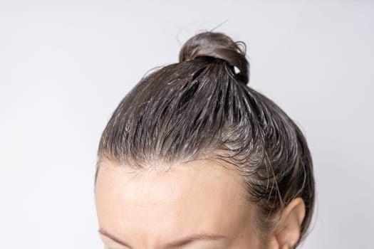 Close-up of a woman's heClose-up of a woman's head in the process of hair coloring on a white background. Closeup woman hands dyeing hair using a brush. Colouring of white hair at home.