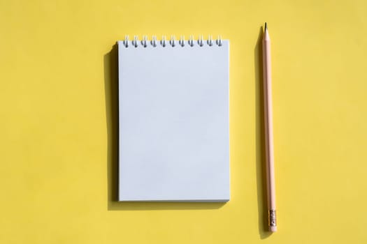 Open notepad and pencil or pen on yellow background. Composition of writing to-dos for the day. The notebook lies on a plain background with space for writing.