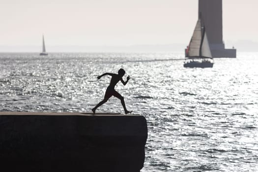 A boy in swimming trunks scatters on the pier before jumping into the water - monochrome image. Mid shot