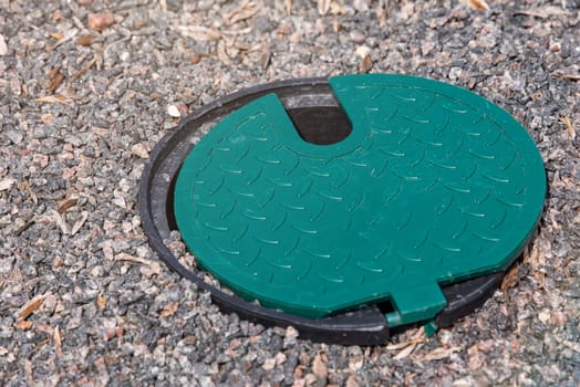 A plastic hatch in the garden covering the connection point for the irrigation hose. A protective hatch in the garden for connecting water and watering plants. High quality photo