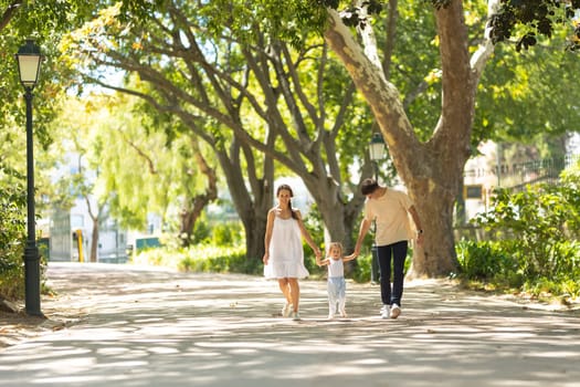 A little girl with her parents walking in the park holding hands. Mid shot