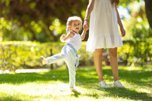 A little girl walking in the park holding her mother by hand. Mid shot