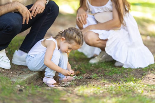 Family in park - a little girl looking down on the grass and her parents watching her. Mid shot