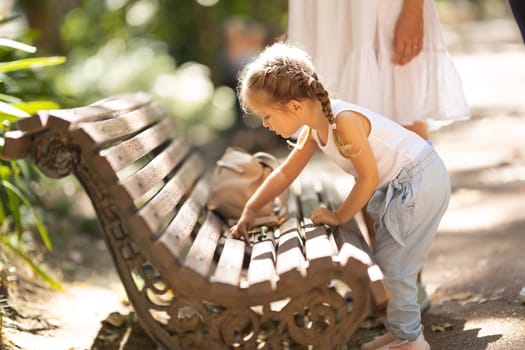 A little girl inspects a bench in a summer park. Mid shot