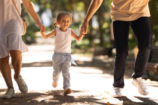 Young and happy family walking in a summer park holding hands. Mid shot