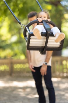 Daughter's father rides his daughter on a swing in a summer park. Mid shot