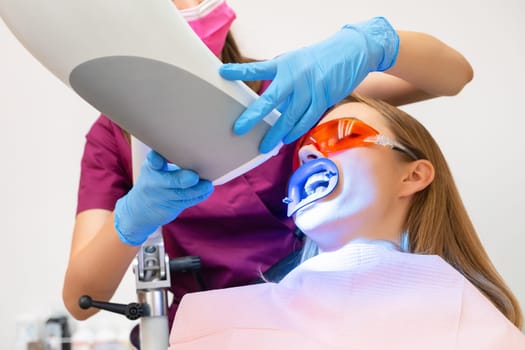 A woman undergoes teeth whitening and the application of a UV lamp for the bleaching process.