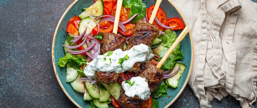 Grilled skewer meat beef kebabs on sticks served with fresh vegetables salad on plate on rustic concrete background from above. Traditional Middle Eastern and Turkish dish Kebab