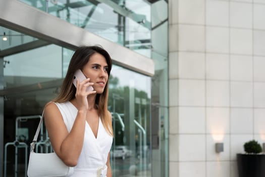 Businesswoman talking on mobile phone near office building. Female entrepreneur during business conversation on cellphone. Woman manager making phone call before meeting