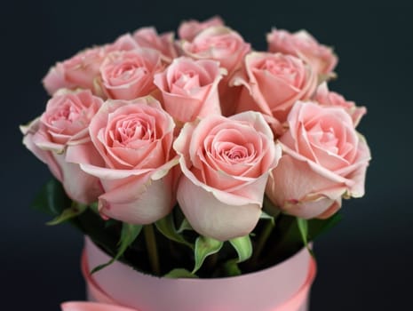 A stunning display of soft pink roses arranged elegantly in a round white box, accented by fresh green leaves, ideal for celebrations or heartfelt gifts.