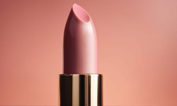 A close-up of a pink lipstick tube is photographed against a soft, peach background. The lipstick is closed and the tube is mostly in focus